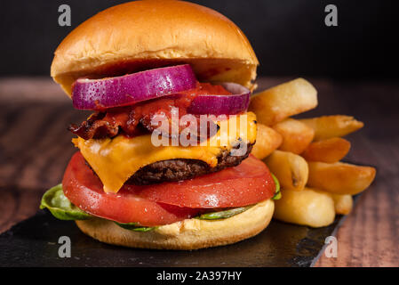 Bacon Cheeseburger mit Salat Tomate Zwiebel auf einem dunklen Hintergrund und Brioche bun Stockfoto