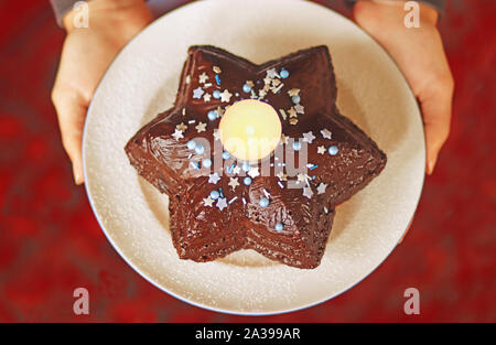 Weibliche Hände halten ein Weihnachten Kuchen in Sternform mit einer brennenden Kerze in der Mitte, Ansicht von oben Stockfoto