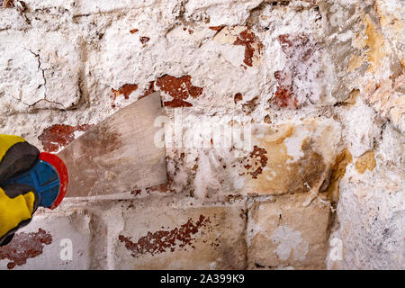 Entfernen alter Farbe von der Wand mit einem Metallspachtel. Kleine Malerarbeiten zu Hause. Hellen Hintergrund. Stockfoto