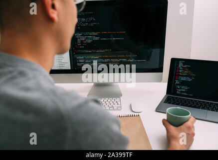 Programmierer, die Arbeit hinter dem Schreibtisch, die Analyse von Code auf dem schwarzen Bildschirm. Stockfoto