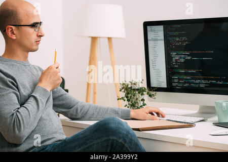 Programmierer, die Arbeit hinter dem Schreibtisch, die Analyse von Code auf dem schwarzen Bildschirm. Stockfoto