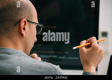 Programmierer, die Arbeit hinter dem Schreibtisch, die Analyse von Code auf dem schwarzen Bildschirm. Stockfoto