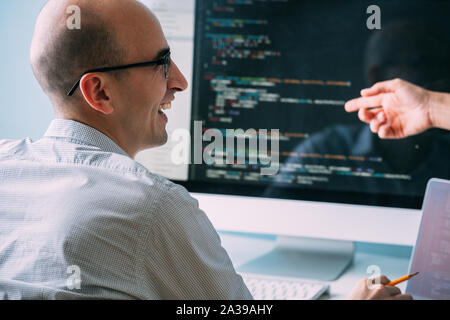 Programmierer, die Arbeit hinter dem Schreibtisch, Analyse der Code beim Chatten mit Kollegen Stockfoto