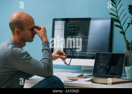 Programmierer, die Arbeit hinter dem Schreibtisch, die Analyse von Code auf dem schwarzen Bildschirm. Stockfoto