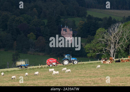 Ein Blick in Richtung Craigievar Castle in Aberdeenshire mit Weide und ein Bauer Pressen von Heu im Vordergrund. Stockfoto