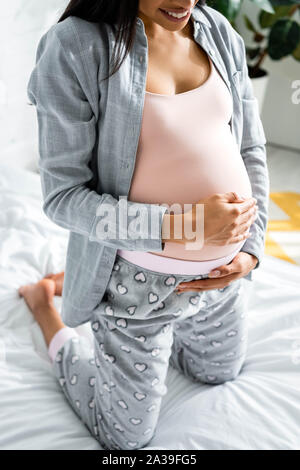 7/8-Ansicht der afrikanischen amerikanischen schwangere Frau im Schlafanzug Bauch umarmen Stockfoto