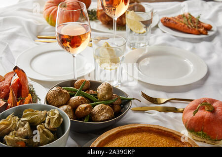 Gebackene Kartoffel und Physalis in der Nähe von Gläsern mit Rose Wein und Zitronensaft Wasser auf weißen Tischdecke Stockfoto