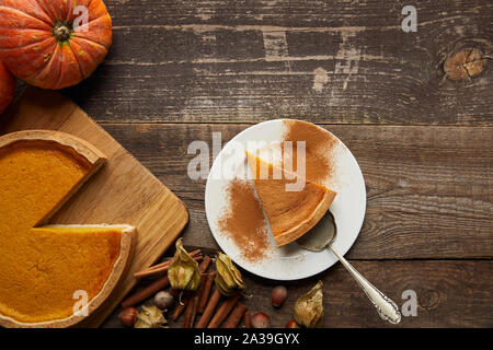 Blick von oben auf die Pumpkin Pie mit zimtpulver in der Nähe der ganzen Kürbis und Gewürzen auf dunklen Holz- Oberfläche Stockfoto