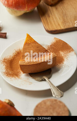 Selektiver Fokus der köstlichen Pumpkin Pie mit zimtpulver auf Platte mit Spachtel auf weißem Marmor tisch Stockfoto