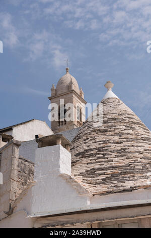 Blick auf den Glockenturm der Kirche von St. Lucia, hinter einem Trullo Haus in Alberobello, Apulien, Italien. Ein UNESCO Weltkulturerbe. Stockfoto