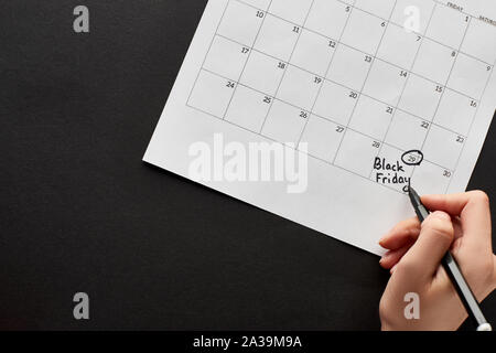 Teilweise mit Blick auf die Frau, die Kennzeichnung der schwarze Freitag Datum im Kalender auf schwarzem Hintergrund Stockfoto