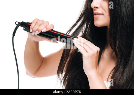 7/8-Ansicht von lächelnden brunette schöne Frau glätten Lange glänzendes Haar mit Bügeleisen isoliert auf weißem Stockfoto