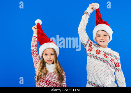 Vorderansicht des Zwei lächelnde Kinder in Pullover und Nikolausmützen isoliert auf Blau Stockfoto