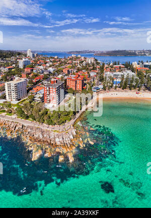 Berühmten Manly Beach in Sydney Northern Beaches mit weit entfernten Hafen von Sydney und CBD Türme über Horizont in Antenne vertikale Ansicht von pazifischen Gewässern surfen Stockfoto