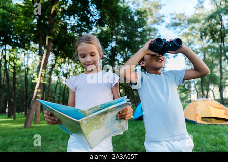 Glückliches Kind bei map in der Nähe von African American Boy auf der Suche nach durch ein Fernglas Stockfoto