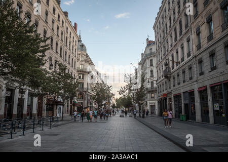 LYON, Frankreich - 14. JULI 2019: Fußgänger gehen auf die Rue de la Republique Straße in Lyon, Frankreich, in der Abenddämmerung mit Blick auf Haussmann Stil Gebäude und commer Stockfoto