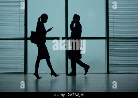 Silhouetten von Menschen zu Fuß in Airport Terminal, am Telefon sprechen und texting Stockfoto