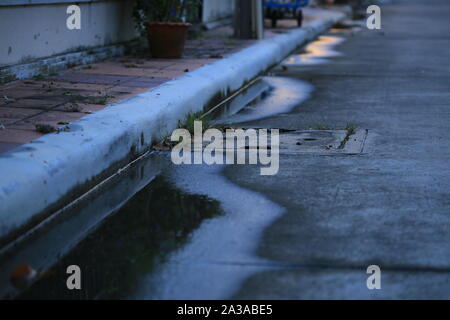 Wasser Pfütze auf der Straße. schlechte Drainage System links Wasser in der Nähe von auffangbecken ablassen Einlass auf eine konkrete Straße. Schmale konkrete Bausteine zu Wanderweg kleine Stockfoto