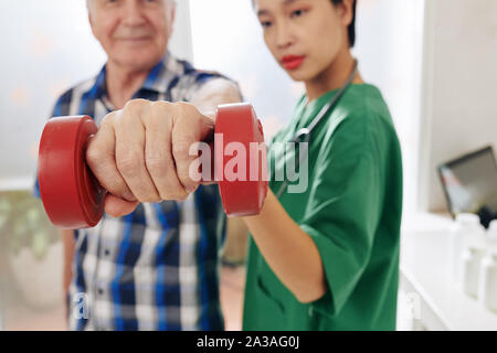 Lächelnd älterer Mann Übungen mit Hanteln unter Kontrolle der Krankenschwester Stockfoto