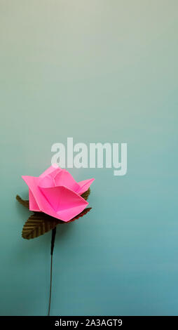 Ein rosa Papier Rose, auf einem blauen Hintergrund mit Farbverlauf. Stockfoto