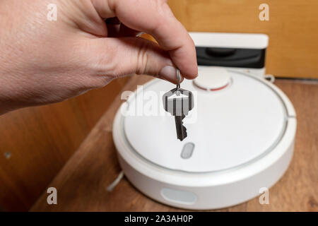 Männliche hand mit einer Taste auf dem Hintergrund des Roboter-Staubsaugers Stockfoto