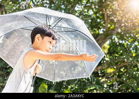 Kid hand Regenschirm spielen auf der Natur. Kleiner Junge versteckt sich unter einem Regenschirm. glückliches Kind fangen Regentropfen. Gerne lustig Kind genießen Stockfoto