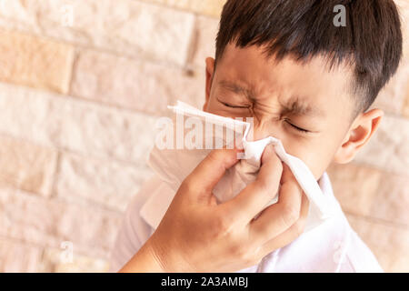 Eltern helfen, einem Kind die Nase in die Luft zu sprengen. Asiatische little boy blasen Nase mit einem Taschentuch zu Hause Stockfoto