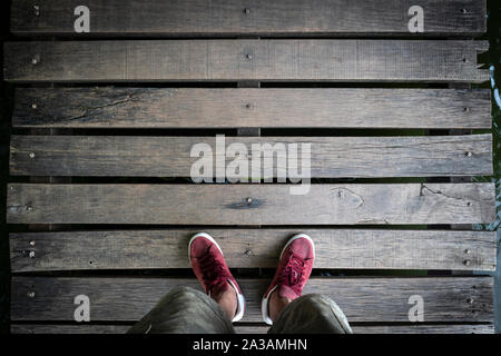 Ein Mann mit roten Sneakers stehen auf einer Holzbrücke. Blick von oben auf die alte Holz Tafel Brücke Hintergrund. Stockfoto