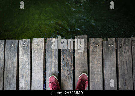 Ein Mann mit roten Sneakers stehen auf einer Holzbrücke. Blick von oben auf die alte Holz Tafel Brücke Hintergrund. Stockfoto