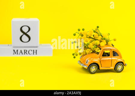 Moskau, Russland - 23. Februar, 8. März 2019: Internationaler Tag der Frau Karte mit Spielzeug Modell der retro Auto Lieferung Blumenstrauß von Mimosa Blumen auf Gelb Stockfoto