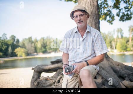 Mann, kariertes Hemd sitzt in der Nähe von Tree Stockfoto