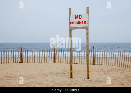 Auf dem Schild am Strand im Ashbury Park steht „kein Schwimmen“. An der Ostküste der USA ist aufgrund des Klimawandels eine erhöhte Stranderosion und mehr Flecken mit rauem Wetter und Küstenüberflutungen aufgetreten. Stockfoto