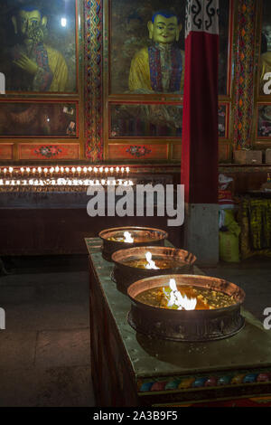 Yak butter Kerzen brennen als Opfer vor einem Buddha Statue im Kloster Ganden auf Wangbur Mountain in der Nähe von Lhasa, Tibet, gegründet 1409 A.D. Stockfoto