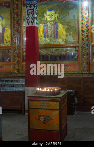 Yak butter Kerzen brennen als Opfer vor einem Buddha Statue im Kloster Ganden auf Wangbur Mountain in der Nähe von Lhasa, Tibet, gegründet 1409 A.D. Stockfoto