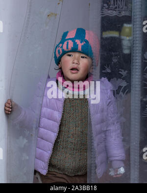 Eine junge tibetische Junge in einer Strickmütze und Fell sieht aus der Familie Shop in einer Nachbarschaft, in Lhasa, Tibet. Stockfoto