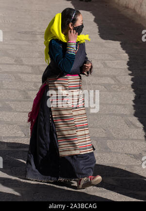 Eine tibetische Frau pilgrim in traditioneller Kleidung, einschließlich ihrer farbenfrohen bangdian oder pangden Schürze, besucht das Kloster Drepung in der Nähe von Lhasa, Tibet. Stockfoto