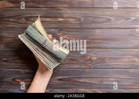 Weibliche hand mit einem großen und dicken Bündel von verschiedenen Dollar Banknoten auf Holz- Hintergrund. Lohn- und Gehaltszahlung Konzept mit kopieren. Stockfoto