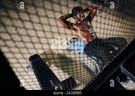 Verschwitzten schwarzen jungen Mann hart arbeiten, wenn Sie Sit-ups auf gym Sitzbank, Ansicht von oben Stockfoto