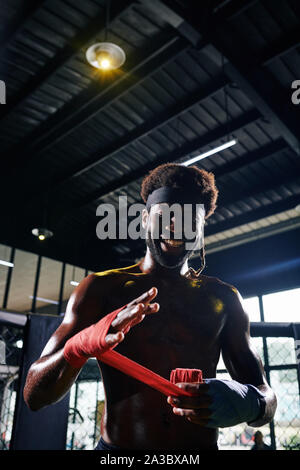 Lächelnd Schwarz Muay Thai Boxer wickeln Handgelenke mit Binde sie während der Schulung zu schützen. Stockfoto