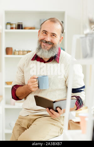 Portrait von bärtigen älteren Mann fröhlich lächelnd an Kamera, während Sie bei einer Tasse Kaffee am Morgen Stockfoto