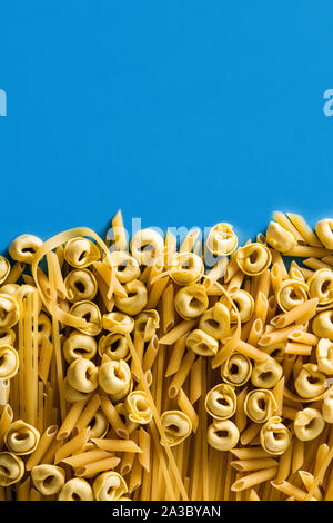Verschiedene Arten von Pasta. Penne Pasta, Ravioli, Tortellini und capellini auf blauem Hintergrund Stockfoto