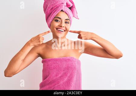 Junge schöne Frau mit Handtuch Dusche nach Badewanne über isoliert weißer Hintergrund lächelt Fröhlich angezeigt und zeigen mit den Fingern Zähne und mout Stockfoto