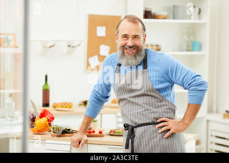 Taille bis Portrait von bärtigen älteren Mann mit Schürze auf Kamera vergnügt, während zu Hause kochen, kopieren Raum Stockfoto