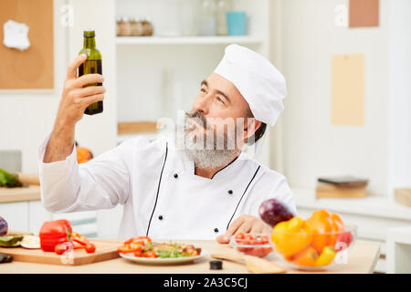 Portrait von bärtigen Senior Chef holding Olivenöl Flasche beim Kochen Fleisch im Restaurant Küche, Kopie Raum Stockfoto
