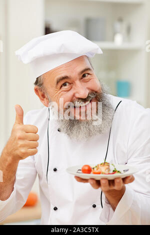 Portrait von fröhlichen Senior Chef präsentiert schöne italienische Gericht und zeigt den Daumen nach oben, während im Restaurant Küche posing Stockfoto