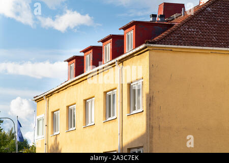 Bunte gelb Stadthaus mit roten Dachgauben in einem ziegeldach in einer teilweisen Nahaufnahme vor einem blauen bewölkten Himmel Stockfoto