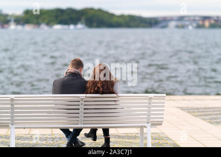 Paar auf einer Bank sitzen mit Blick auf kabbelwasser an einem kalten und windigen Herbsttag in ihren dicken Mänteln in einer Ansicht von hinten Stockfoto