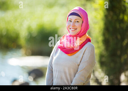 Attraktive selbstbewusste Frau im hijab stand draußen in den sonnigen Sommertag, glücklich lächelnd. Muslimische Frau lifestyle Konzept Stockfoto