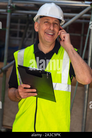 Männliche builder Vorarbeiter, Mitarbeiter, Auftragnehmer oder Architekt auf der Baustelle halten Schwarze Zwischenablage und über sein Mobiltelefon Stockfoto