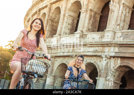 Zwei glückliche junge Frauen Freunde Touristen mit Fahrrädern am Kolosseum in Rom, Italien bei Sonnenaufgang.